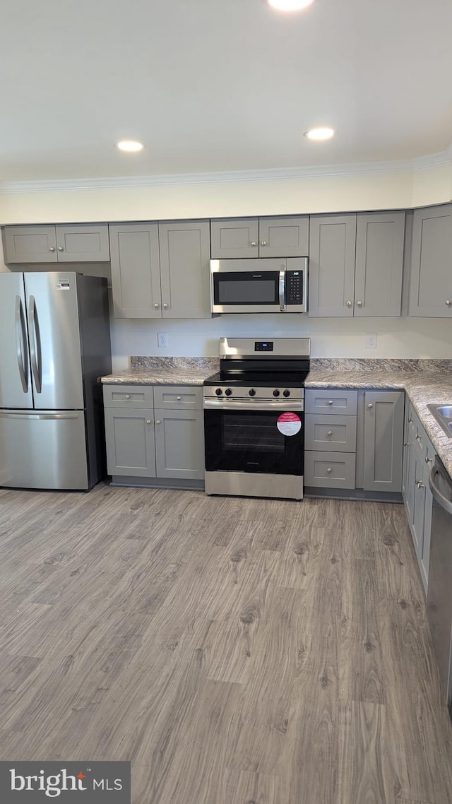 kitchen with crown molding, gray cabinets, appliances with stainless steel finishes, light wood-style floors, and light stone countertops