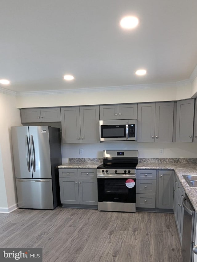 kitchen with light wood-type flooring, appliances with stainless steel finishes, crown molding, and gray cabinetry