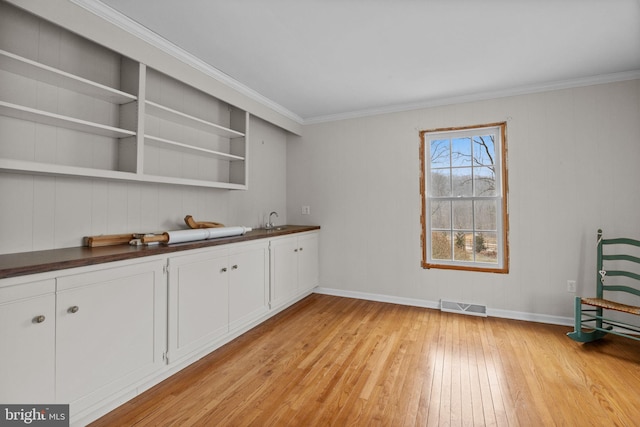 bar with sink, light wood-type flooring, white cabinetry, and ornamental molding