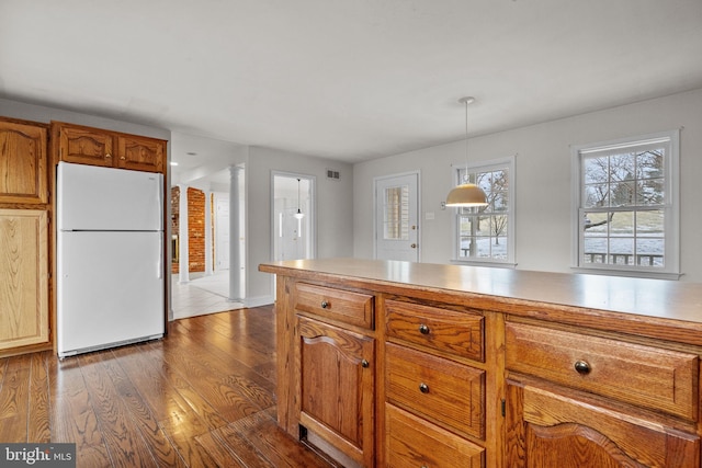 kitchen with white refrigerator, dark wood-type flooring, hanging light fixtures, and ornate columns