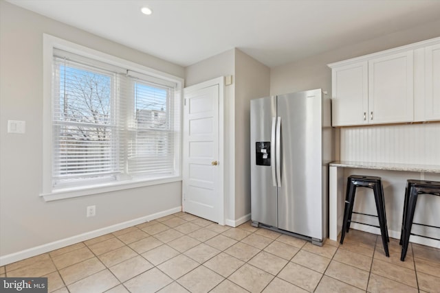 kitchen with white cabinets, light stone counters, stainless steel refrigerator with ice dispenser, and light tile patterned floors