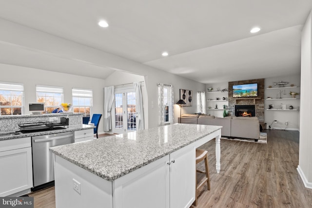 kitchen featuring lofted ceiling, a center island, stainless steel dishwasher, a stone fireplace, and white cabinets