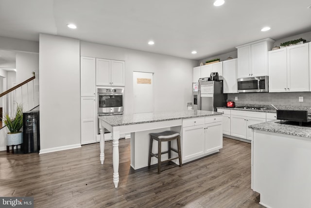 kitchen with a center island, dark wood-type flooring, light stone countertops, appliances with stainless steel finishes, and white cabinets