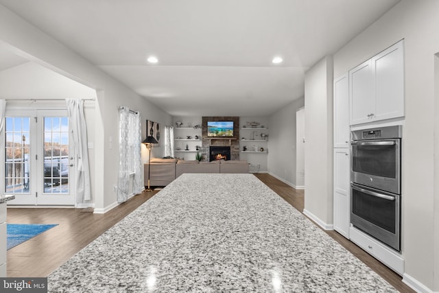 kitchen with light stone counters, stainless steel double oven, and built in shelves