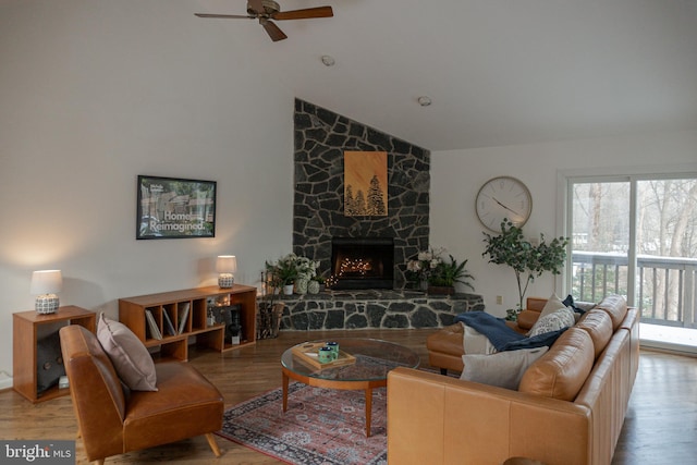 living room with vaulted ceiling, a stone fireplace, and wood finished floors