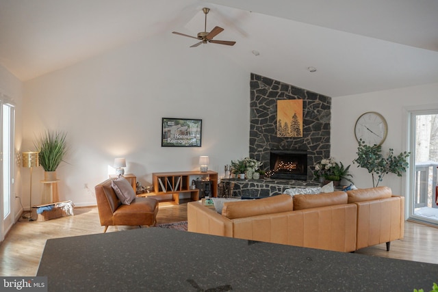 living area with high vaulted ceiling, wood finished floors, and a stone fireplace