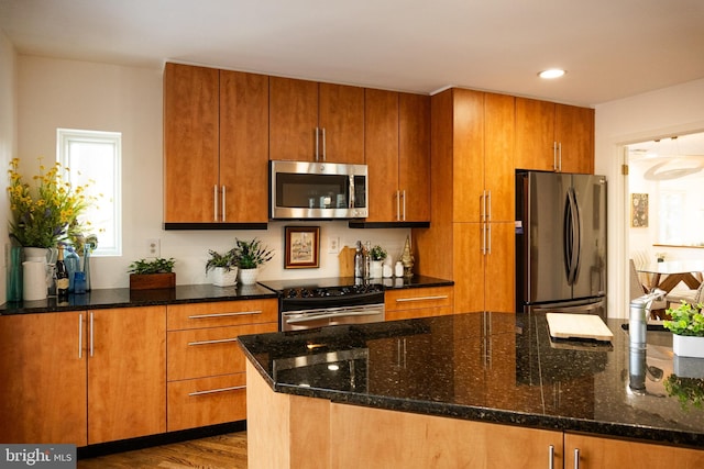 kitchen featuring appliances with stainless steel finishes, dark wood-style flooring, brown cabinetry, and dark stone countertops