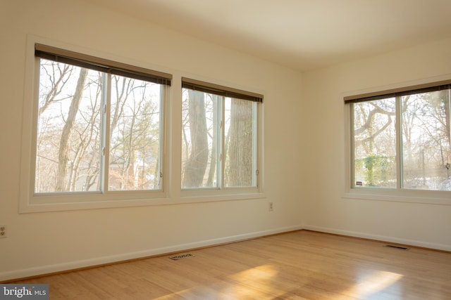 empty room with wood finished floors, visible vents, and baseboards