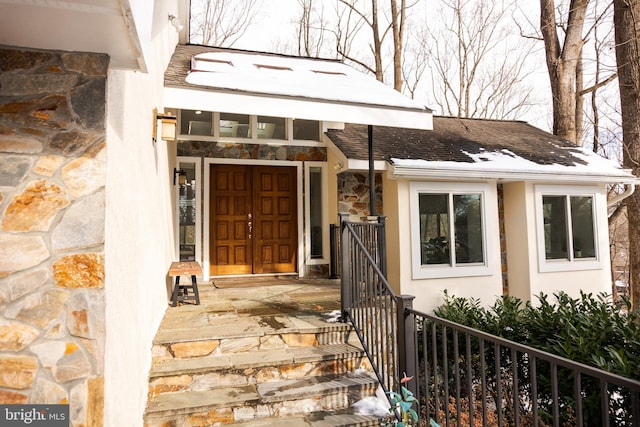 property entrance featuring stone siding, a shingled roof, and stucco siding