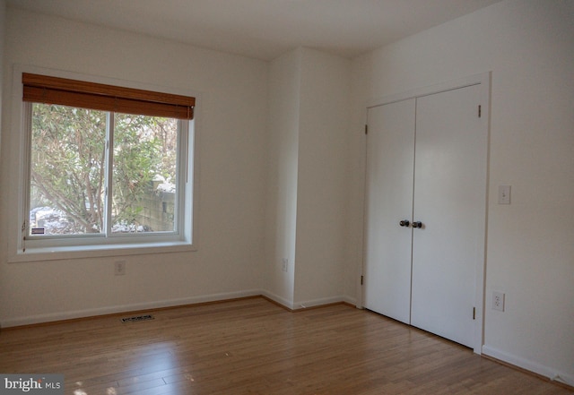 unfurnished bedroom featuring a closet, wood finished floors, visible vents, and baseboards