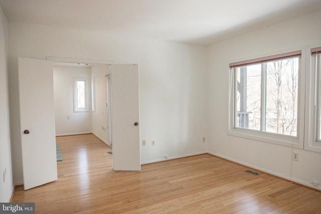 empty room featuring light wood-style flooring, visible vents, and baseboards