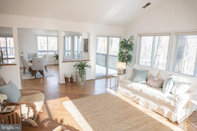 living area featuring lofted ceiling, wood finished floors, visible vents, and a healthy amount of sunlight