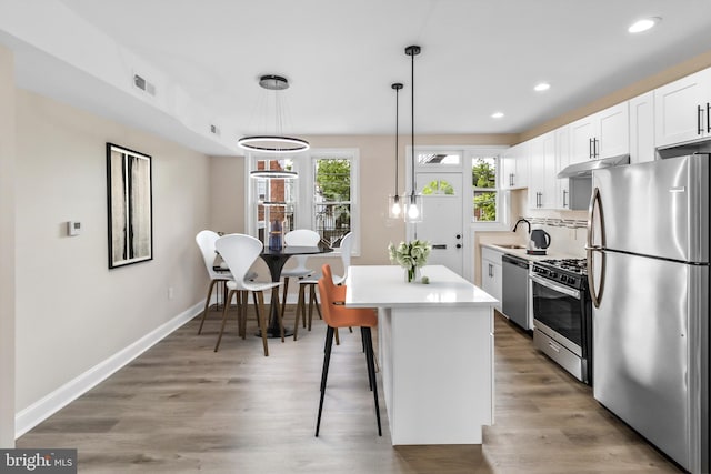 kitchen with stainless steel appliances, sink, white cabinets, tasteful backsplash, and hanging light fixtures