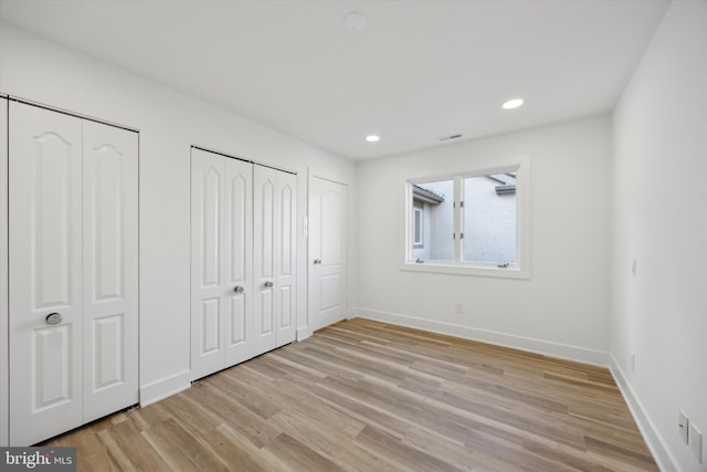 unfurnished bedroom with light wood-type flooring and multiple closets