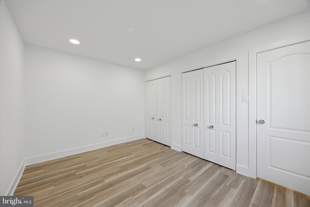 unfurnished bedroom featuring light wood-type flooring and multiple closets