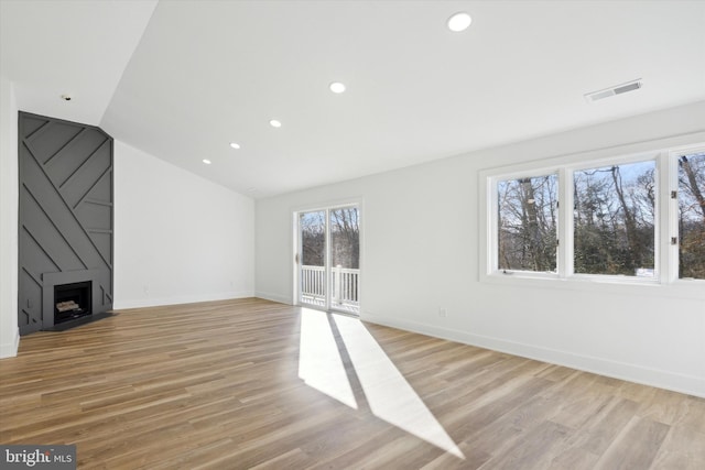 unfurnished living room with lofted ceiling, a large fireplace, and light hardwood / wood-style flooring