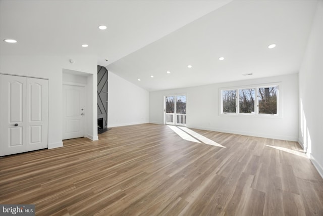 unfurnished living room with lofted ceiling, a large fireplace, and light hardwood / wood-style floors