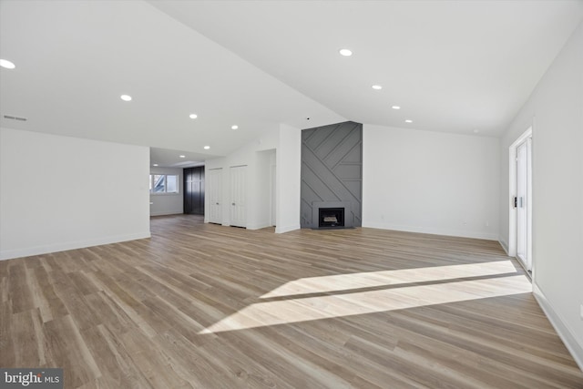 unfurnished living room featuring vaulted ceiling, a large fireplace, and light hardwood / wood-style floors