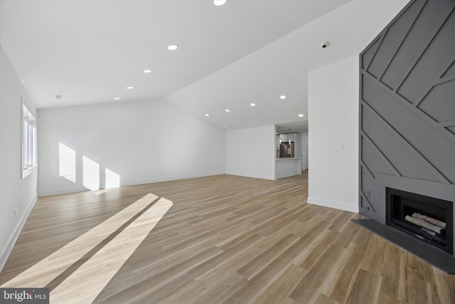 unfurnished living room featuring lofted ceiling, a fireplace, and light wood-type flooring