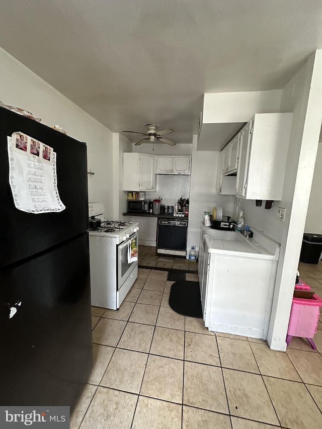 kitchen featuring black appliances, light tile patterned floors, white cabinets, washer / clothes dryer, and ceiling fan