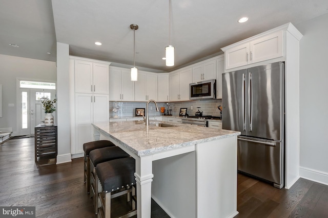 kitchen with light stone countertops, white cabinets, appliances with stainless steel finishes, sink, and hanging light fixtures