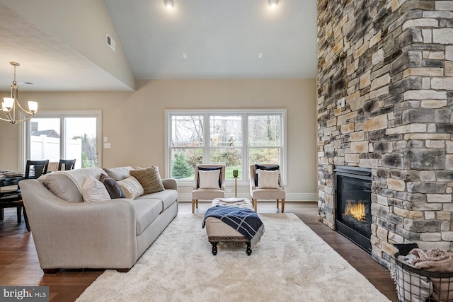 living room with vaulted ceiling, dark hardwood / wood-style floors, a stone fireplace, and a chandelier