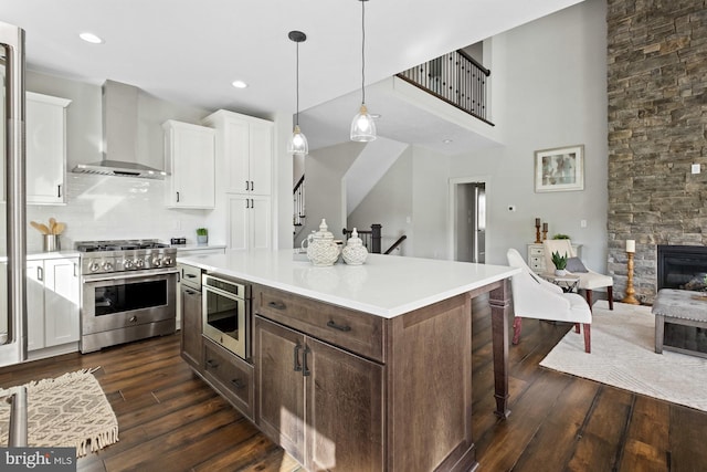 kitchen with wall chimney range hood, pendant lighting, a kitchen island, white cabinetry, and appliances with stainless steel finishes