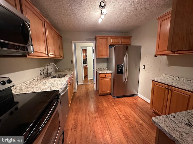 kitchen featuring appliances with stainless steel finishes, light hardwood / wood-style floors, light stone counters, and sink