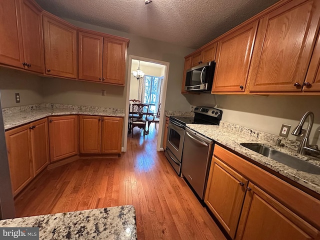 kitchen with stainless steel appliances, sink, a chandelier, light wood-type flooring, and light stone counters