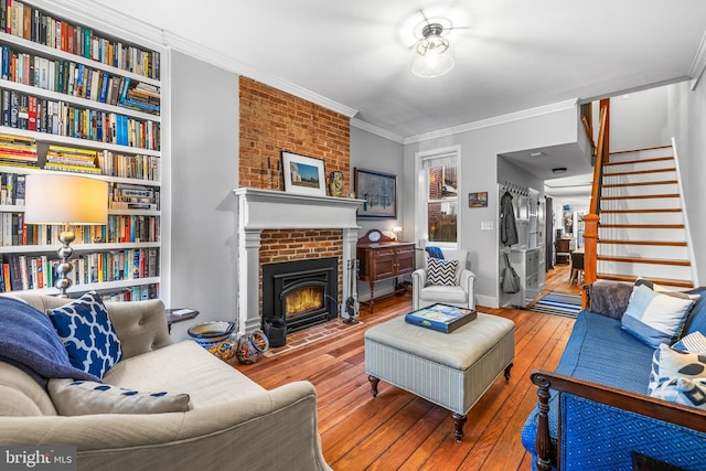 living room featuring built in features, a brick fireplace, ornamental molding, and hardwood / wood-style floors