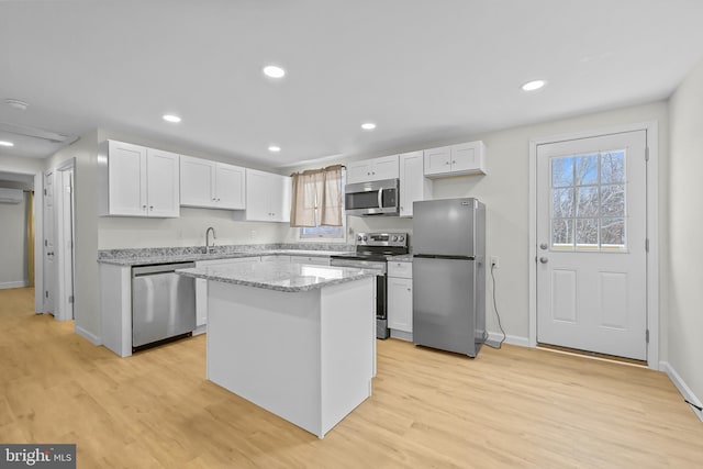 kitchen featuring light stone counters, stainless steel appliances, light hardwood / wood-style floors, a kitchen island, and white cabinets