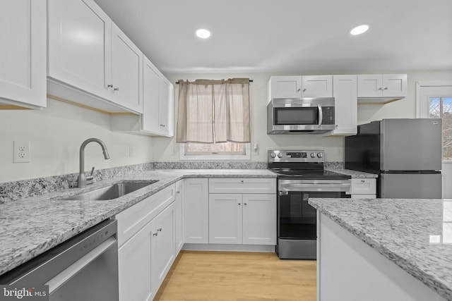 kitchen featuring light stone countertops, light hardwood / wood-style flooring, white cabinetry, appliances with stainless steel finishes, and sink