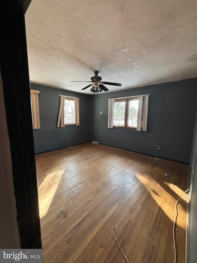 empty room featuring ceiling fan, a textured ceiling, hardwood / wood-style floors, and plenty of natural light