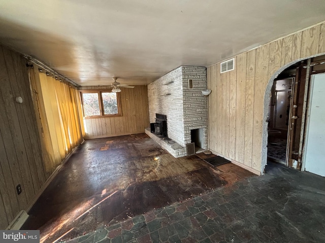 unfurnished living room with ceiling fan, wooden walls, and a stone fireplace