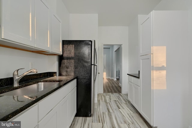 kitchen with sink, white cabinets, dark stone countertops, and stainless steel fridge