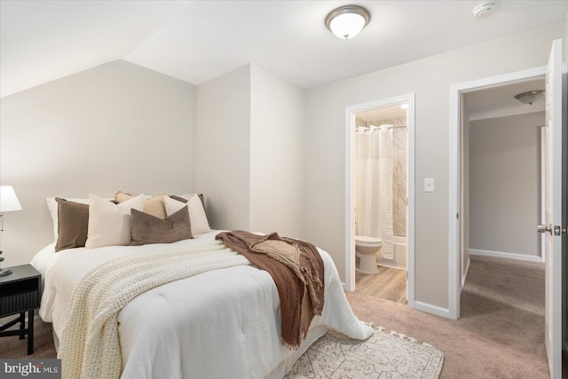 carpeted bedroom featuring ensuite bath and vaulted ceiling