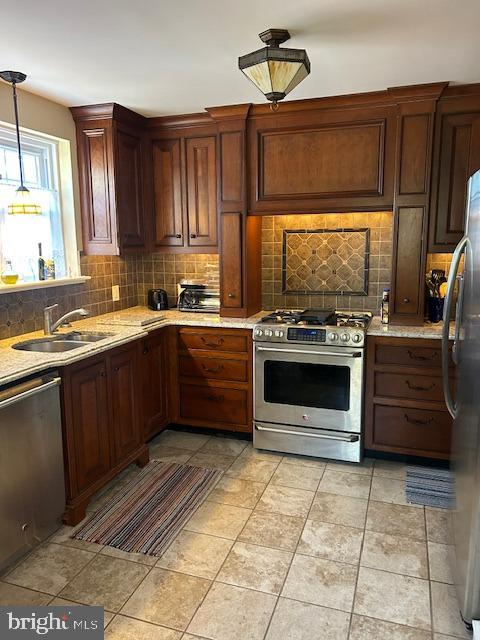 kitchen featuring appliances with stainless steel finishes, decorative backsplash, hanging light fixtures, light stone counters, and sink