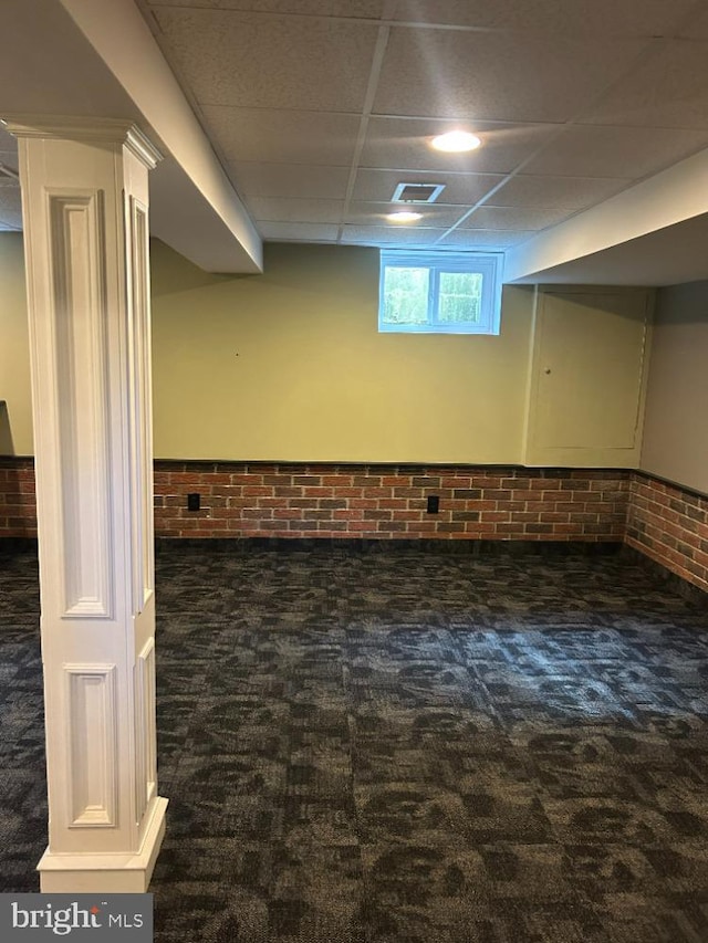 basement with a drop ceiling, brick wall, and dark colored carpet