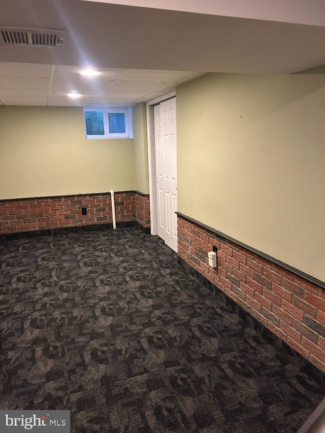 basement featuring dark colored carpet and brick wall