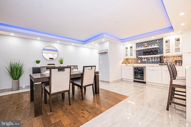 dining space with a tray ceiling, bar area, beverage cooler, and hardwood / wood-style floors