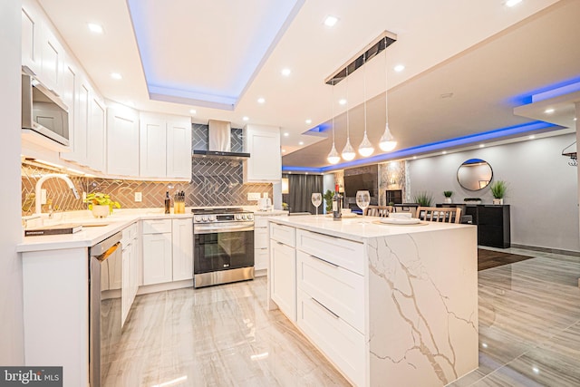 kitchen with wall chimney range hood, white cabinetry, a center island, and appliances with stainless steel finishes