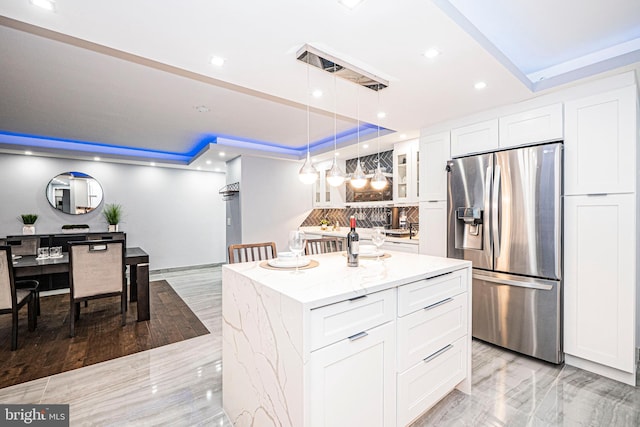 kitchen featuring a center island, light stone countertops, stainless steel fridge with ice dispenser, hanging light fixtures, and white cabinets