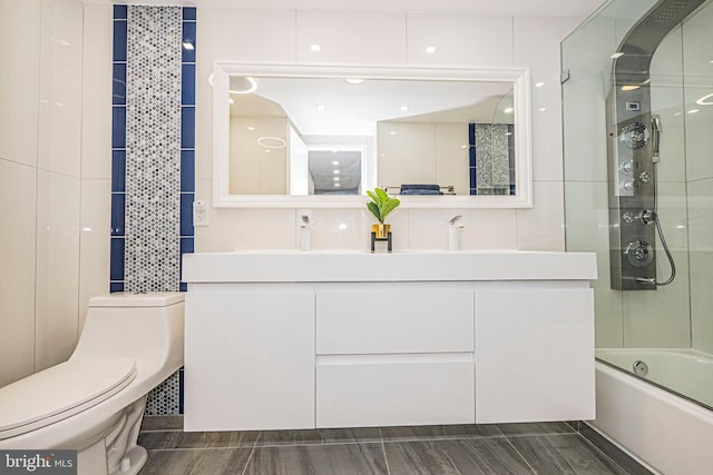 full bathroom with combined bath / shower with glass door, toilet, tile walls, and vanity