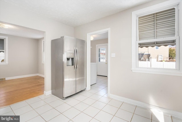 kitchen with a textured ceiling, light tile patterned floors, stainless steel fridge with ice dispenser, and a healthy amount of sunlight