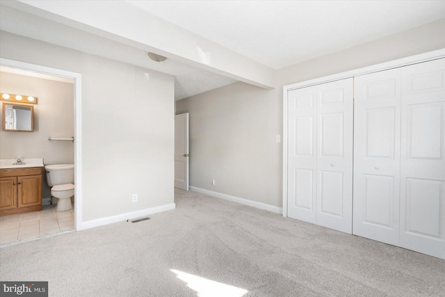 unfurnished bedroom with connected bathroom, light carpet, sink, a closet, and beam ceiling