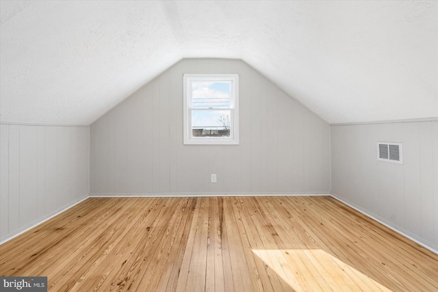 additional living space with a textured ceiling, light hardwood / wood-style flooring, wood walls, and vaulted ceiling