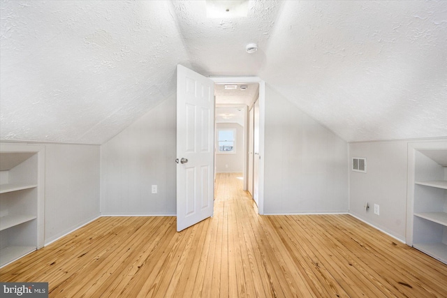 additional living space featuring built in shelves, light hardwood / wood-style flooring, a textured ceiling, and vaulted ceiling