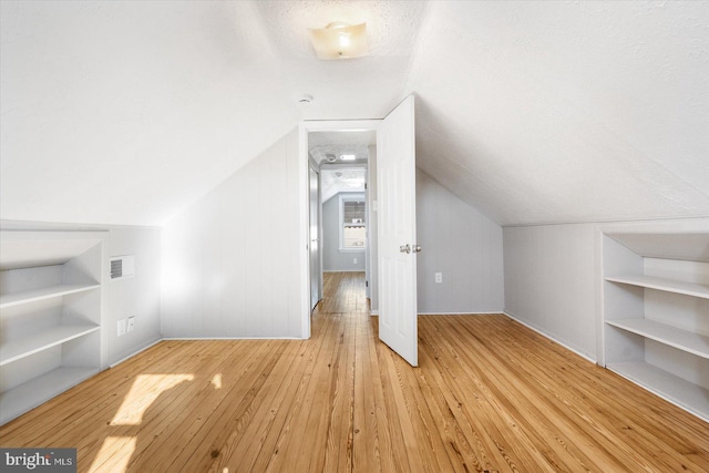 bonus room featuring a textured ceiling, light hardwood / wood-style flooring, and vaulted ceiling