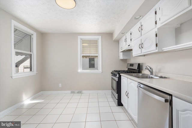 kitchen featuring sink, light tile patterned floors, appliances with stainless steel finishes, a textured ceiling, and white cabinets