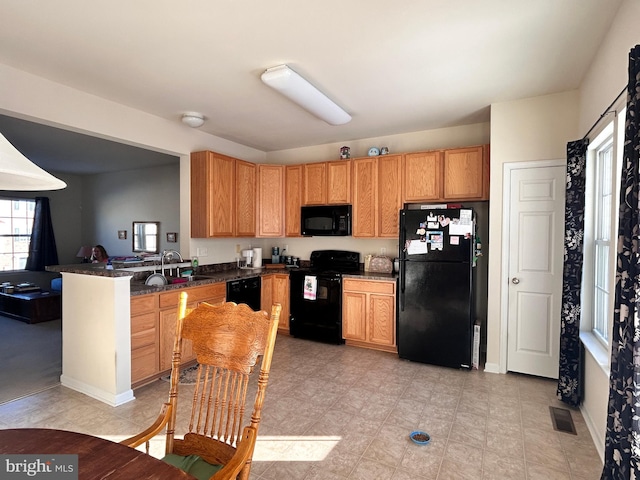 kitchen with black appliances, kitchen peninsula, sink, and dark stone countertops